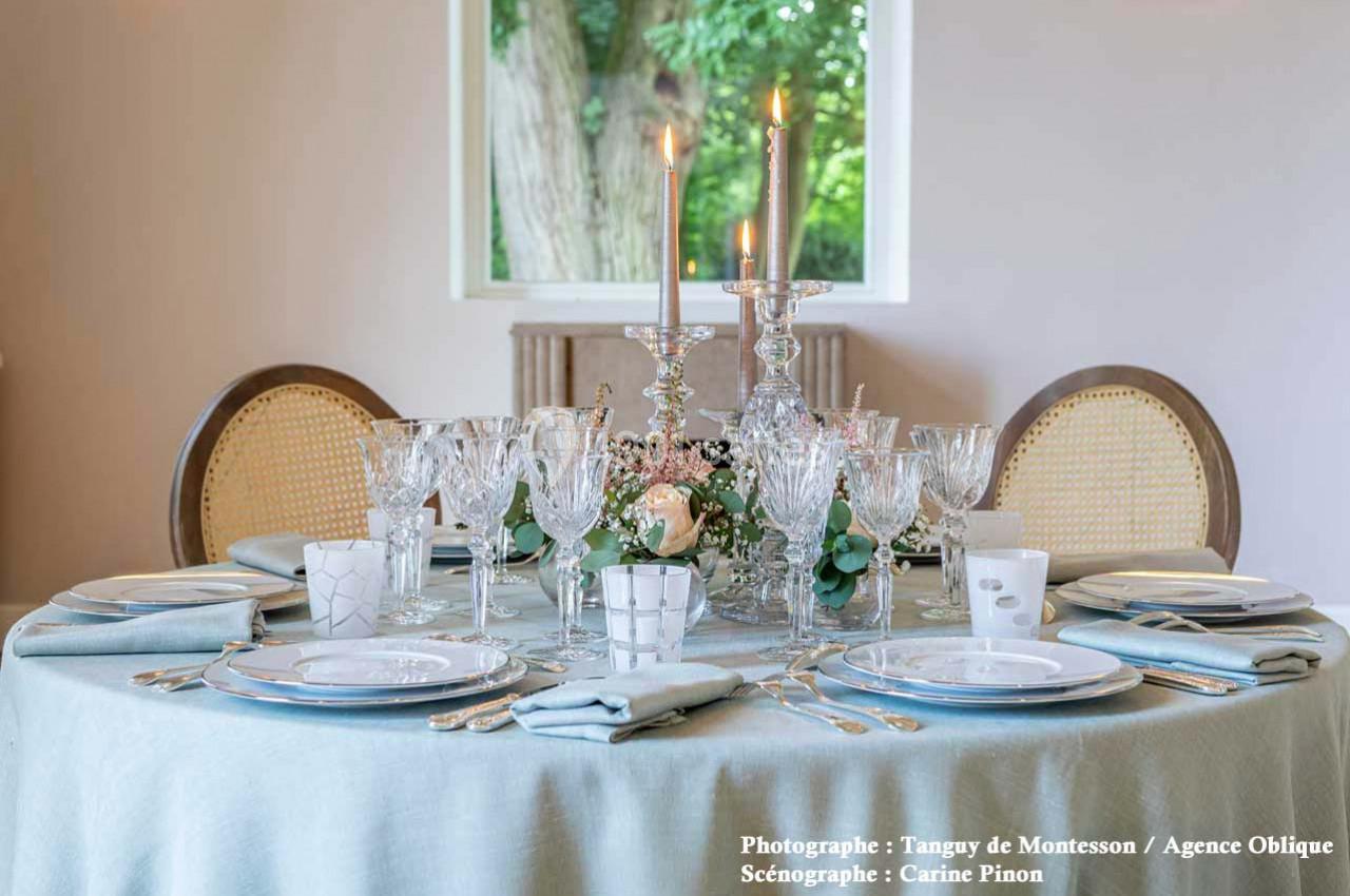 Table élégamment dressée avec nappes bleues, vaisselle raffinée, verres en cristal, chandeliers et décor floral.