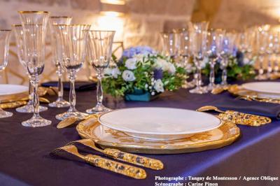Salle lumineuse avec parquet en bois, table ronde dressée avec nappe rouge, et moulures décoratives au plafond.