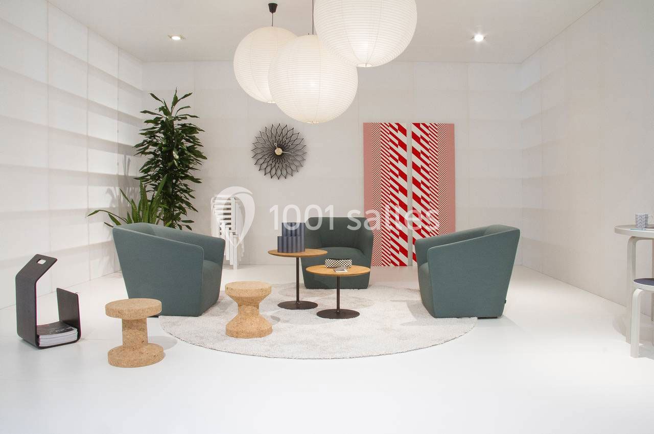 Espace salon moderne avec fauteuils verts, tables basses en bois, tapis rond clair, plantes et décorations murales.