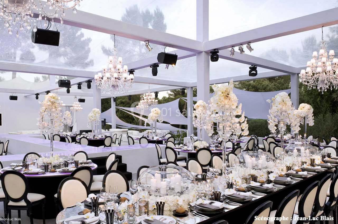 Salle de réception élégante avec tables décorées de fleurs blanches, chandeliers et toit transparent laissant passer la…