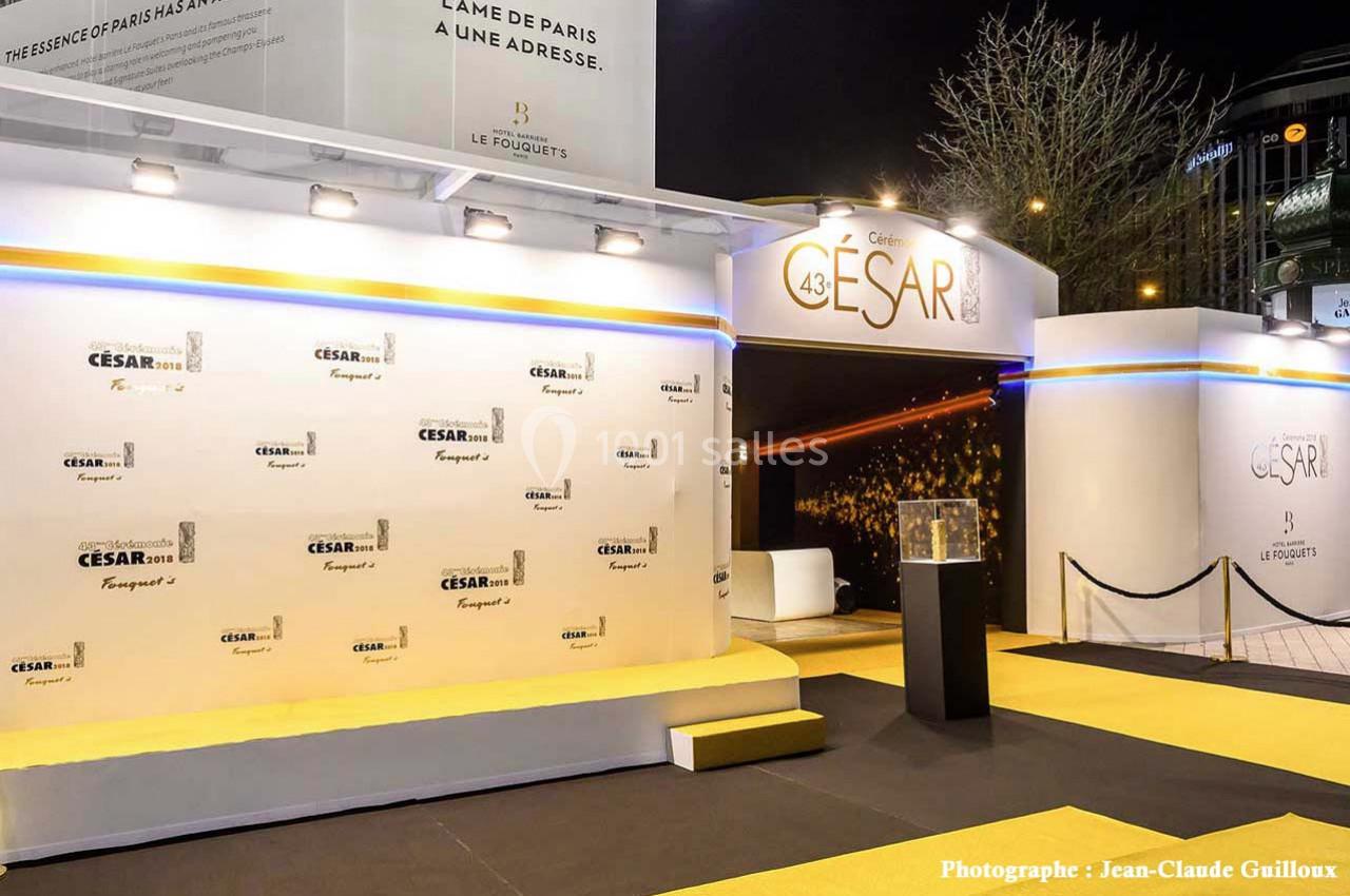 Entrée d'une cérémonie avec tapis jaune, mur de logos ’César’ et décor lumineux en arrière-plan.