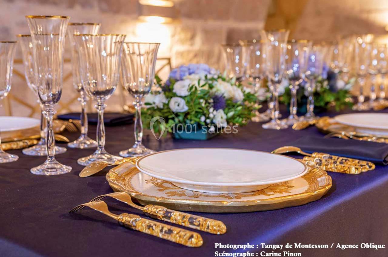 Table élégamment dressée avec vaisselle dorée, verres à pied et centre de table floral dans un décor raffiné.