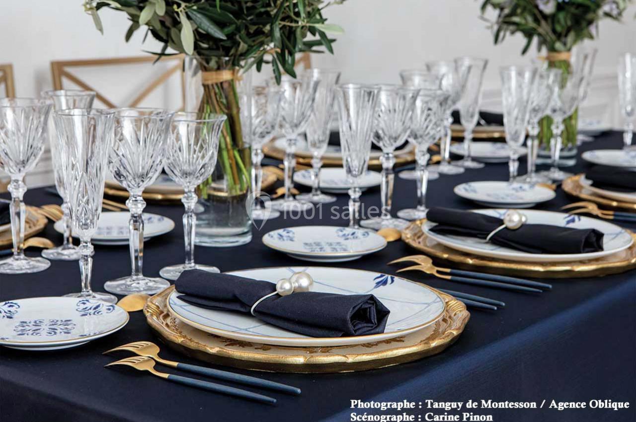Table élégamment dressée avec vaisselle blanche et dorée, couverts dorés, serviettes noires et verres en cristal.