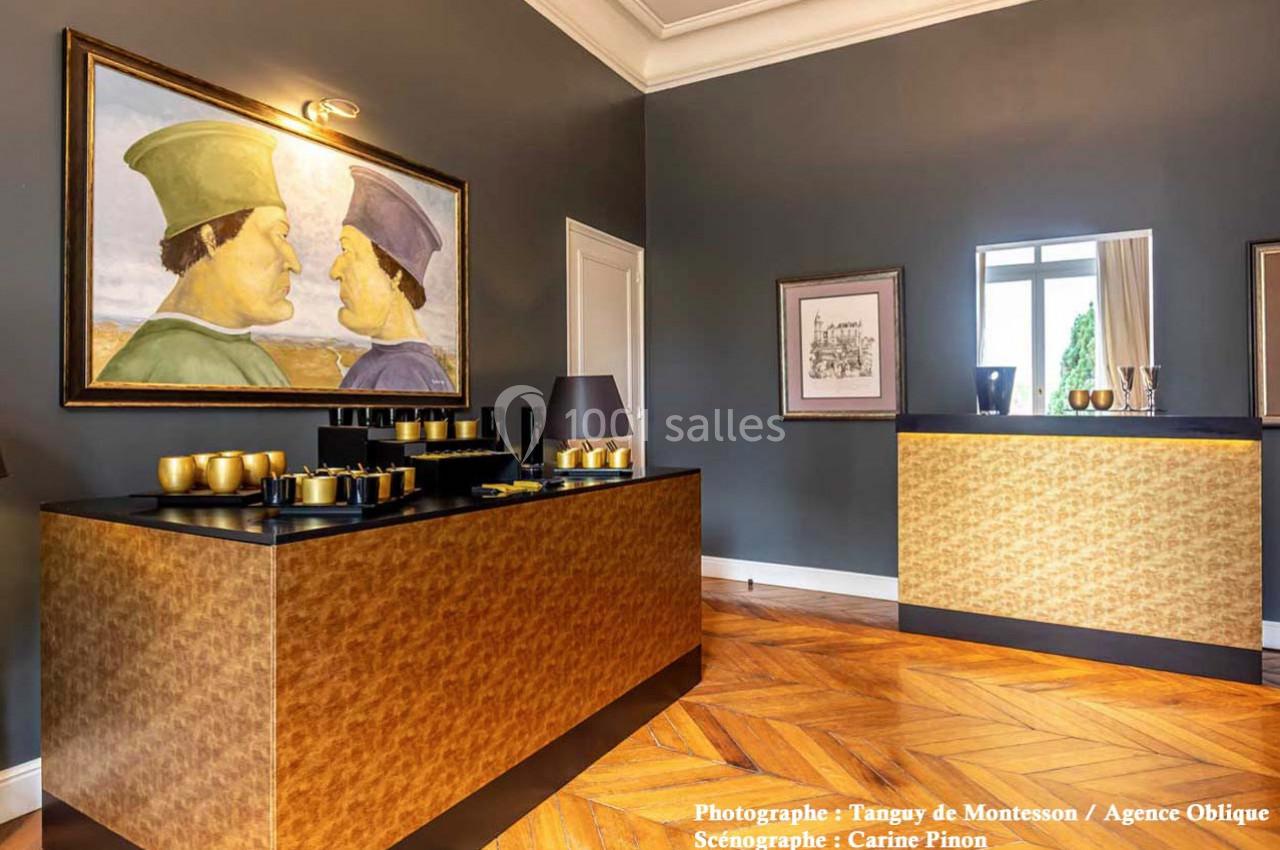 Salle élégante avec parquet en bois, mobilier doré, tableau mural et miroir reflétant une fenêtre lumineuse.