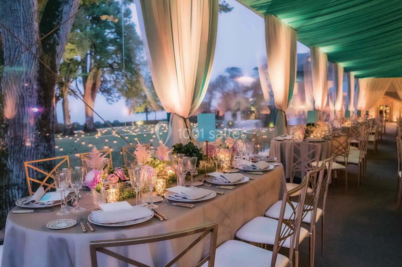 Salle de réception décorée avec des tables élégantes, nappes beiges, chaises dorées et éclairage tamisé.