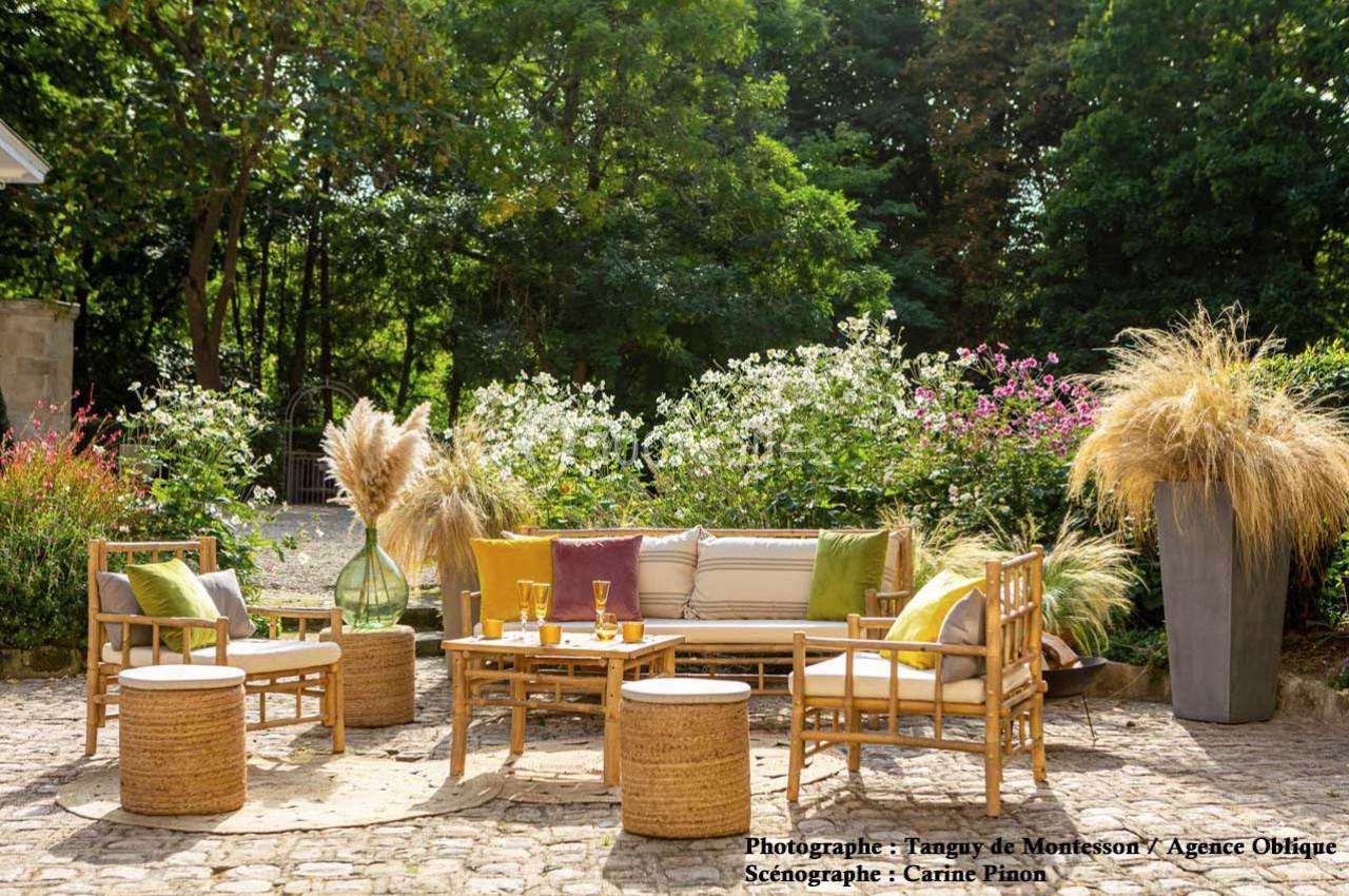 Salon de jardin en rotin avec coussins colorés, entouré de plantes et fleurs, installé sur une terrasse pavée.