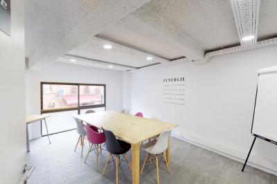 Salle de réunion lumineuse avec table en bois, chaises colorées, tableau blanc et grande fenêtre donnant sur l'extérieur.