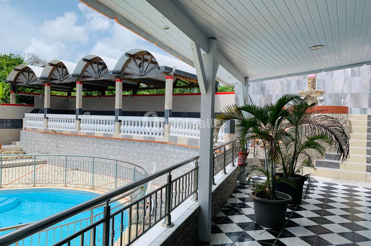 Vue d'une terrasse couverte avec plantes en pot, surplombant une piscine et des structures architecturales modernes.