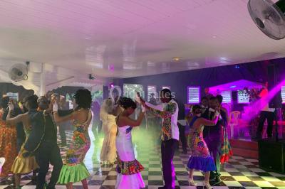 Un couple de mariés danse au centre d'une salle décorée, entouré d'invités applaudissant.