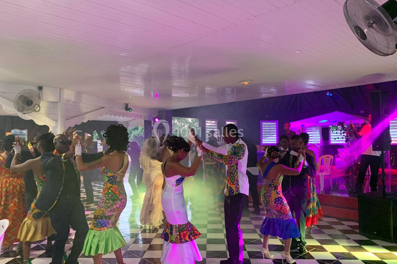 Des couples dansent sur une piste carrelée, entourés de lumières colorées dans une ambiance festive en intérieur.