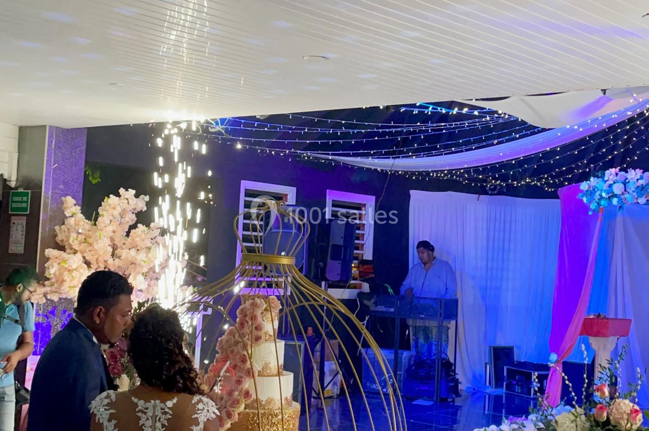 Un couple en tenue de mariage coupe un gâteau décoré, entouré de fleurs et d'une ambiance lumineuse festive.