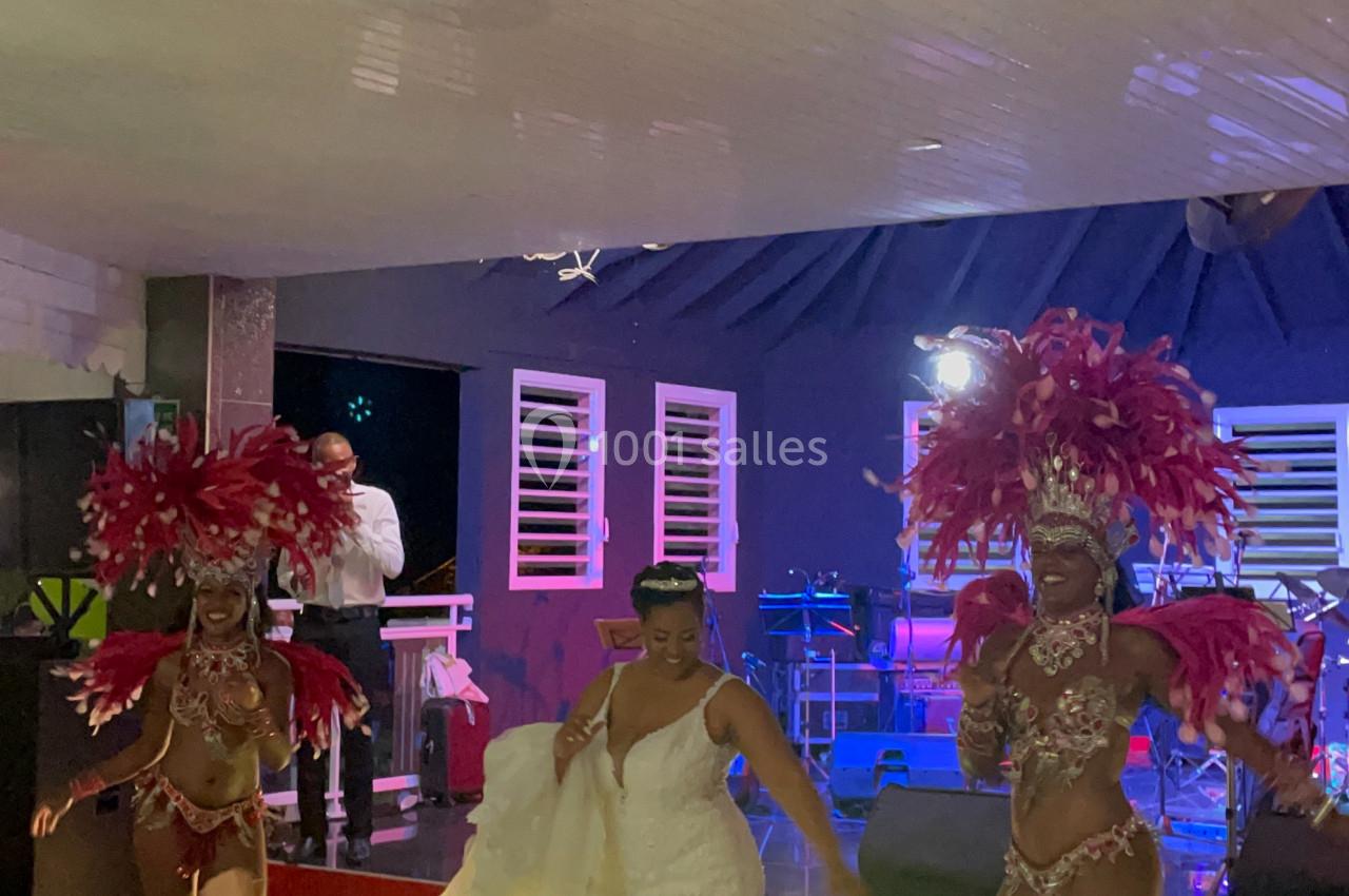 Danseuses en costumes à plumes rouges et une femme en robe blanche sur une scène lors d'une soirée festive.