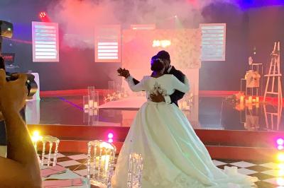 Un couple de mariés danse au centre d'une salle décorée, entouré d'invités applaudissant.