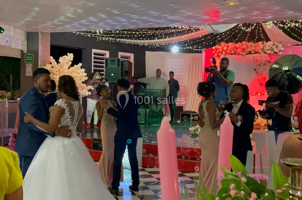 Des couples dansent lors d'une réception de mariage sous une tente décorée de lumières et de fleurs.