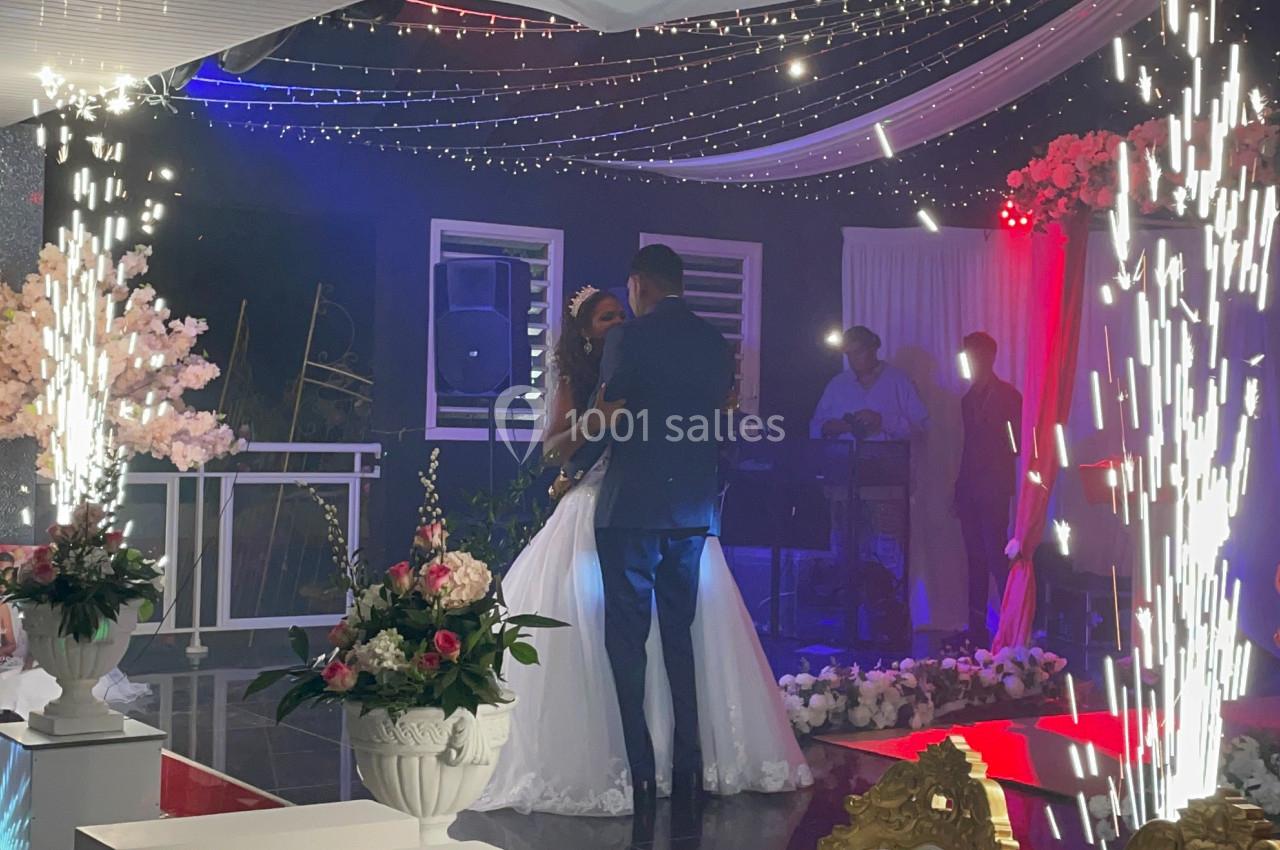 Un couple danse sous des étincelles lors d'une réception de mariage dans une salle décorée de fleurs et de lumières.