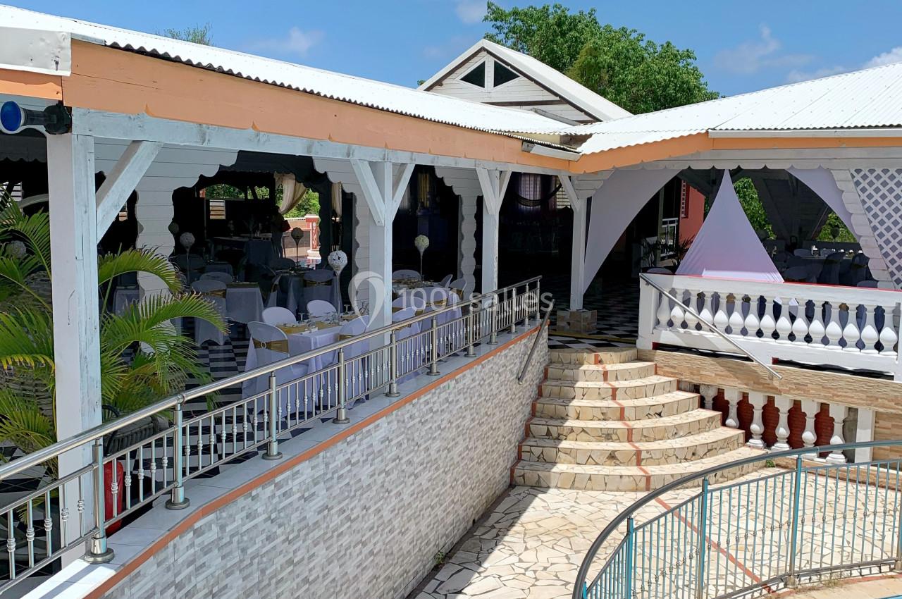 Terrasse extérieure avec tables dressées, escalier en pierre, piscine ronde et ciel dégagé en arrière-plan.