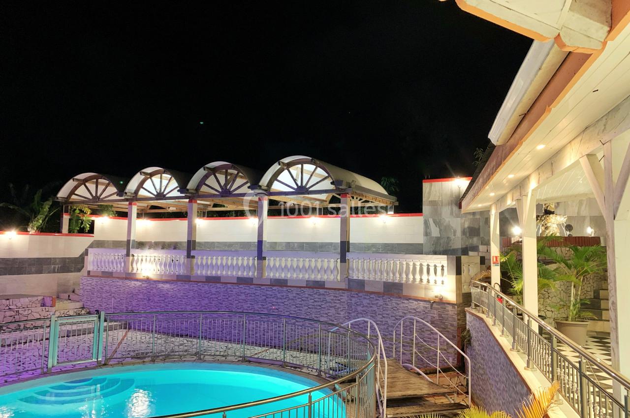 Piscine éclairée de nuit entourée de structures architecturales modernes et d'un bâtiment avec terrasse.