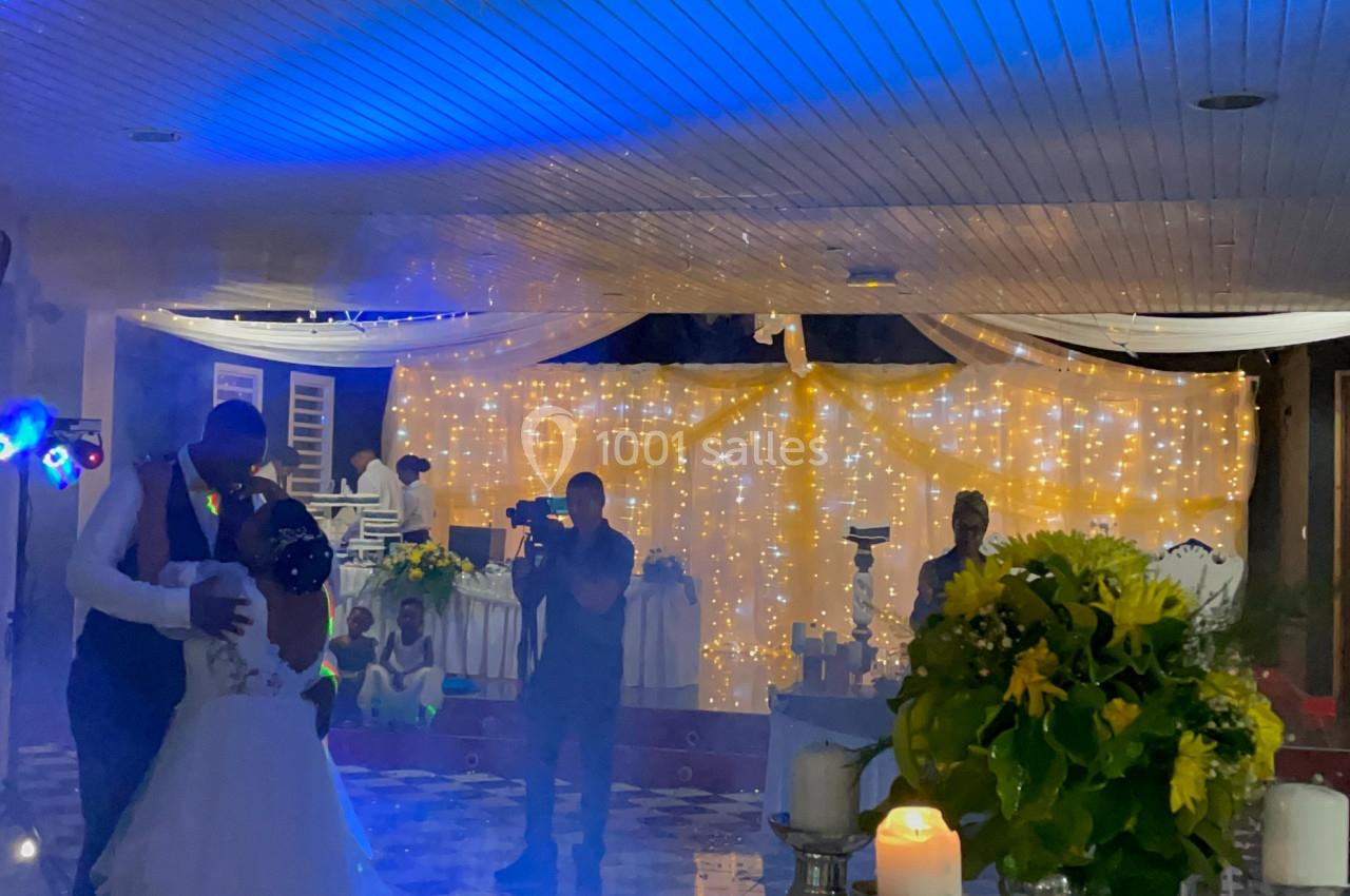 Un couple danse sous des lumières bleues dans une salle décorée avec des guirlandes lumineuses et des fleurs.