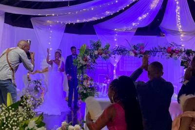 Un couple de mariés danse au centre d'une salle décorée, entouré d'invités applaudissant.