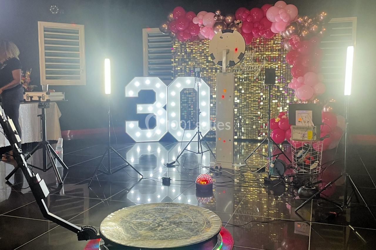 Décoration festive avec ballons roses, chiffre lumineux ’30’, fond scintillant et équipement de photographie.