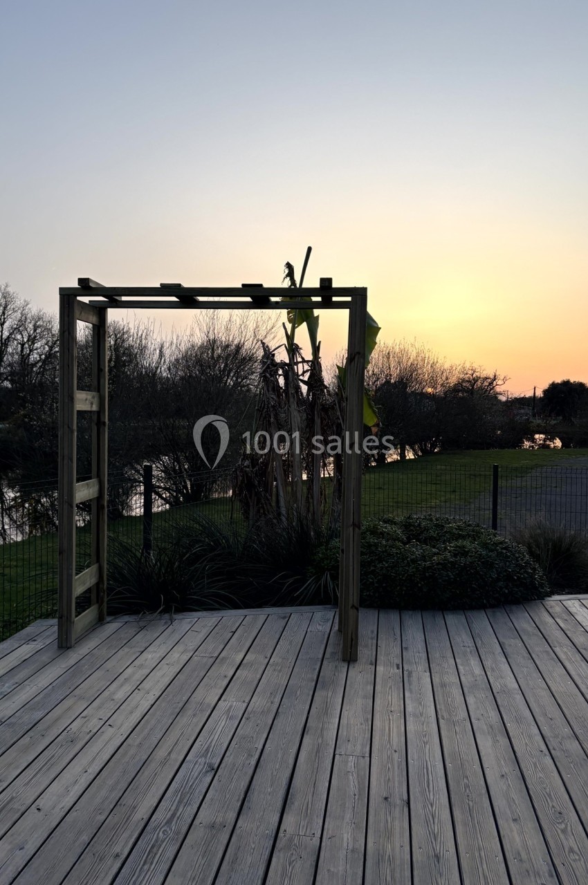 Structure en bois sur une terrasse en bois, avec un coucher de soleil et un paysage naturel en arrière-plan.