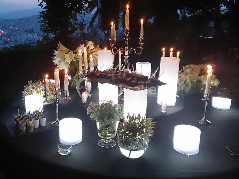 Table décorée pour un dîner en soirée avec chandeliers, bougies, fleurs blanches et vue sur un paysage urbain.