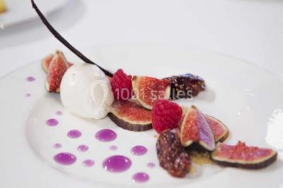Table en bois décorée de fleurs colorées, verres, assiettes et couverts, installée en extérieur sous une tente.