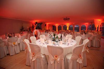 Table en bois décorée de fleurs colorées, verres, assiettes et couverts, installée en extérieur sous une tente.
