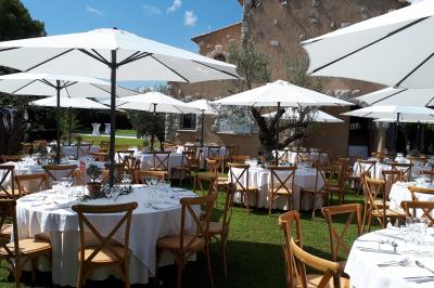 Table en bois décorée de fleurs colorées, verres, assiettes et couverts, installée en extérieur sous une tente.