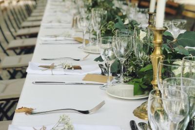 Table en bois décorée de fleurs colorées, verres, assiettes et couverts, installée en extérieur sous une tente.