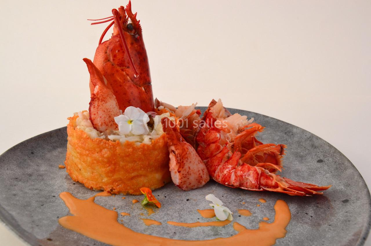 Assiette gastronomique avec homard, risotto crémeux, fleurs comestibles et sauce orangée sur une assiette grise.