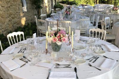 Table en bois décorée de fleurs colorées, verres, assiettes et couverts, installée en extérieur sous une tente.