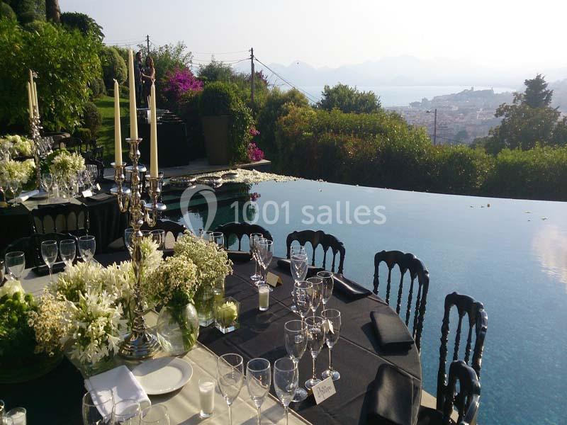 Table dressée élégamment près d'une piscine à débordement, avec vue sur un paysage côtier et des collines verdoyantes.
