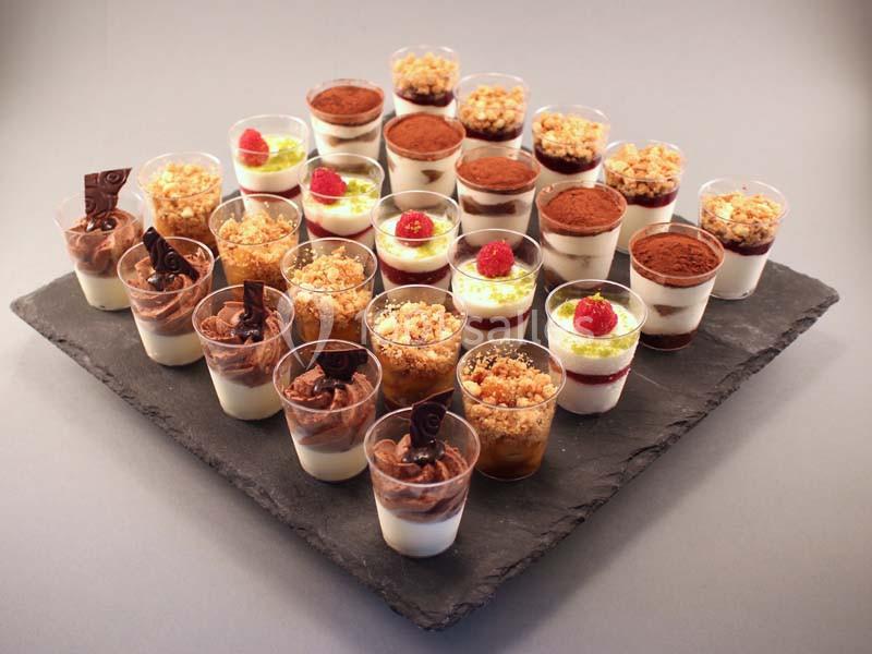 Assortiment de verrines sucrées disposées sur une ardoise, comprenant mousses, crumbles et garnitures variées.