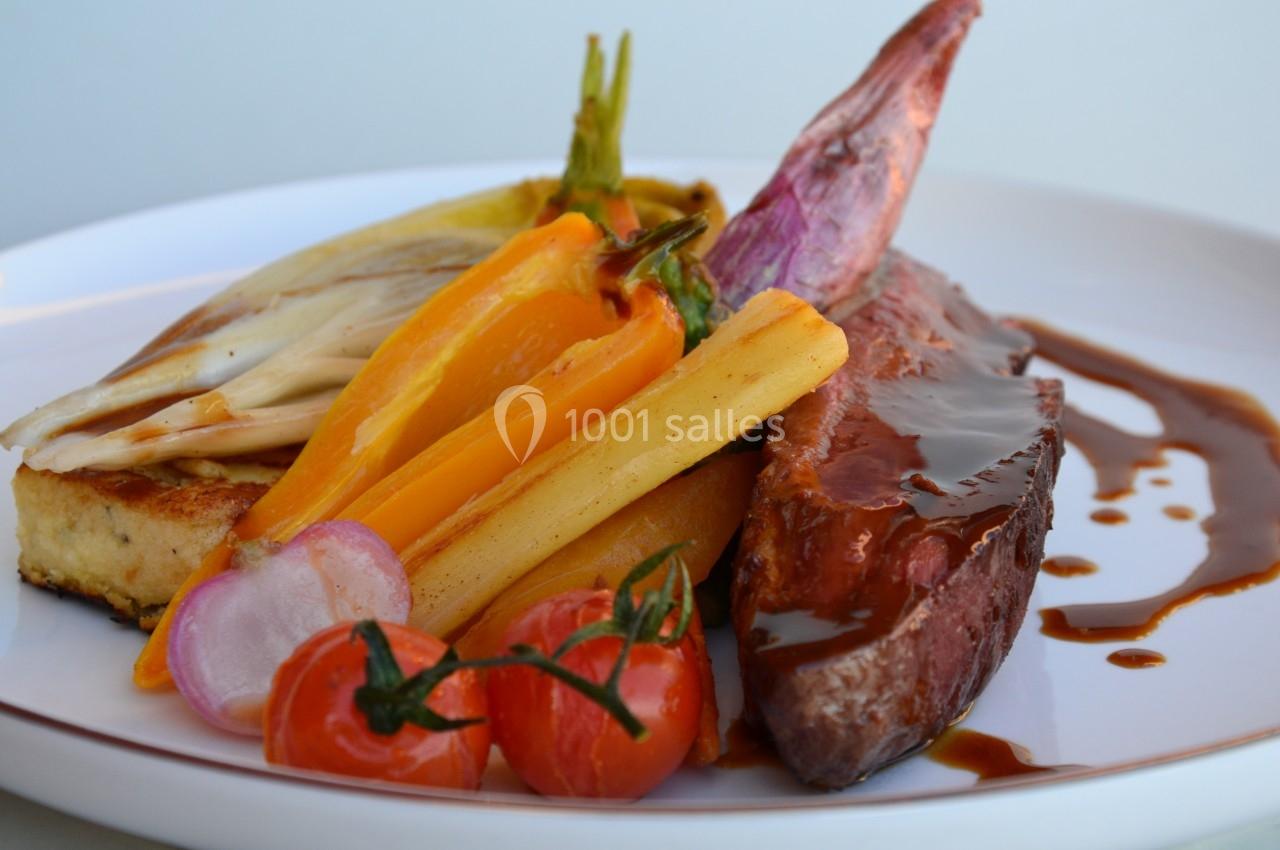 Assiette contenant une pièce de viande nappée de sauce, accompagnée de légumes colorés et d'une tranche de polenta.