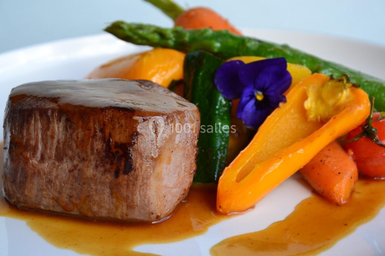 Plat composé d'un filet de viande nappé de sauce, accompagné de légumes colorés et décoré d'une fleur comestible.