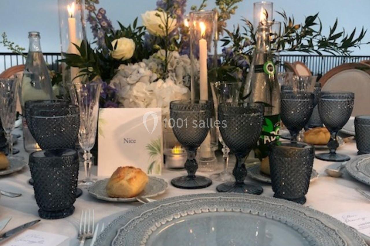 Table élégamment dressée avec vaisselle grise, verres en cristal, chandelles allumées et centre de table floral.