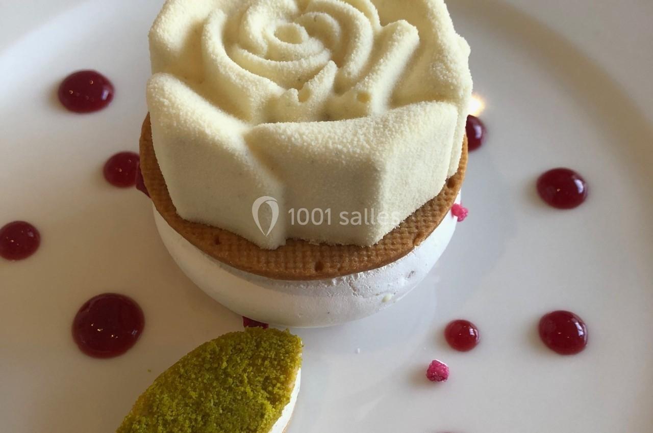 Dessert en forme de rose blanche sur une base de meringue, accompagné de gouttes de coulis rouge et d'une touche verte.