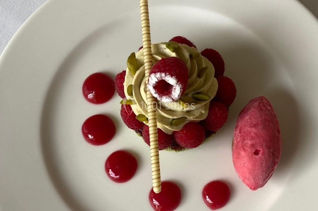 Dessert composé de framboises, crème pistache, décor chocolat, coulis rouge et sorbet framboise sur assiette blanche.