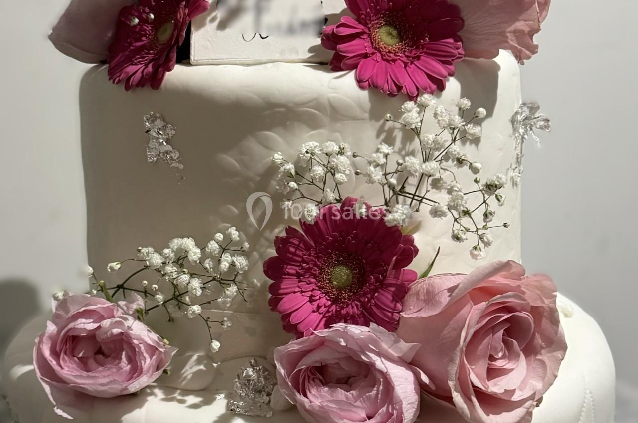 Gâteau de mariage à trois étages décoré de roses roses, de fleurs fuchsia et de gypsophile blanche.