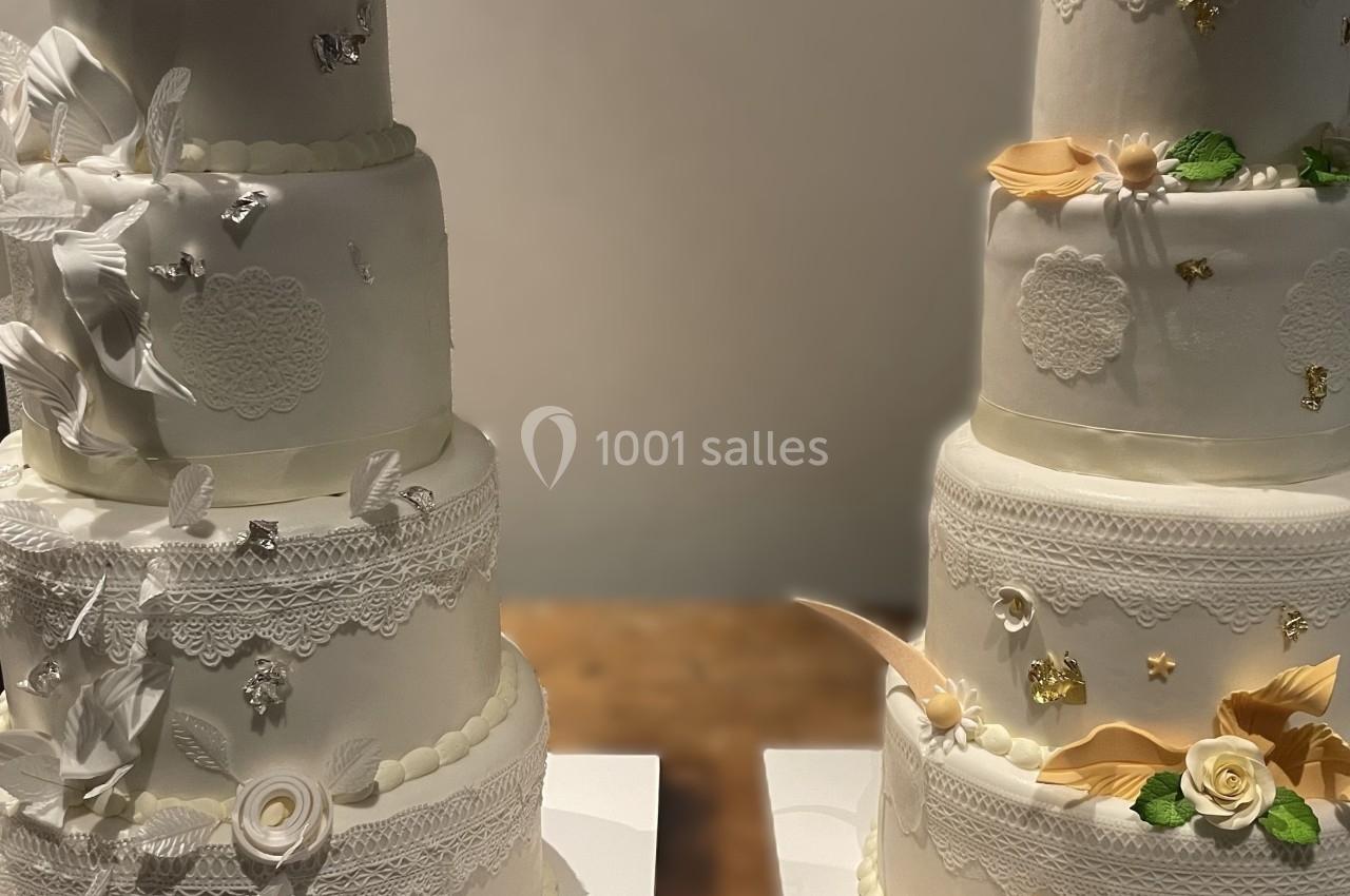 Deux gâteaux de mariage à plusieurs étages décorés de fleurs, dentelles et motifs élégants sur une table.
