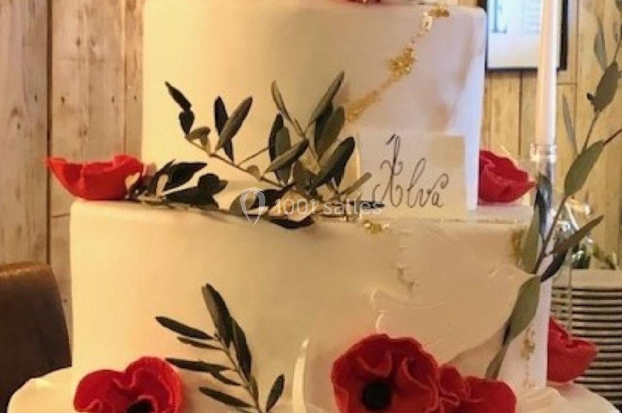 Gâteau de mariage à trois étages décoré de coquelicots rouges, de feuillage et de détails dorés.