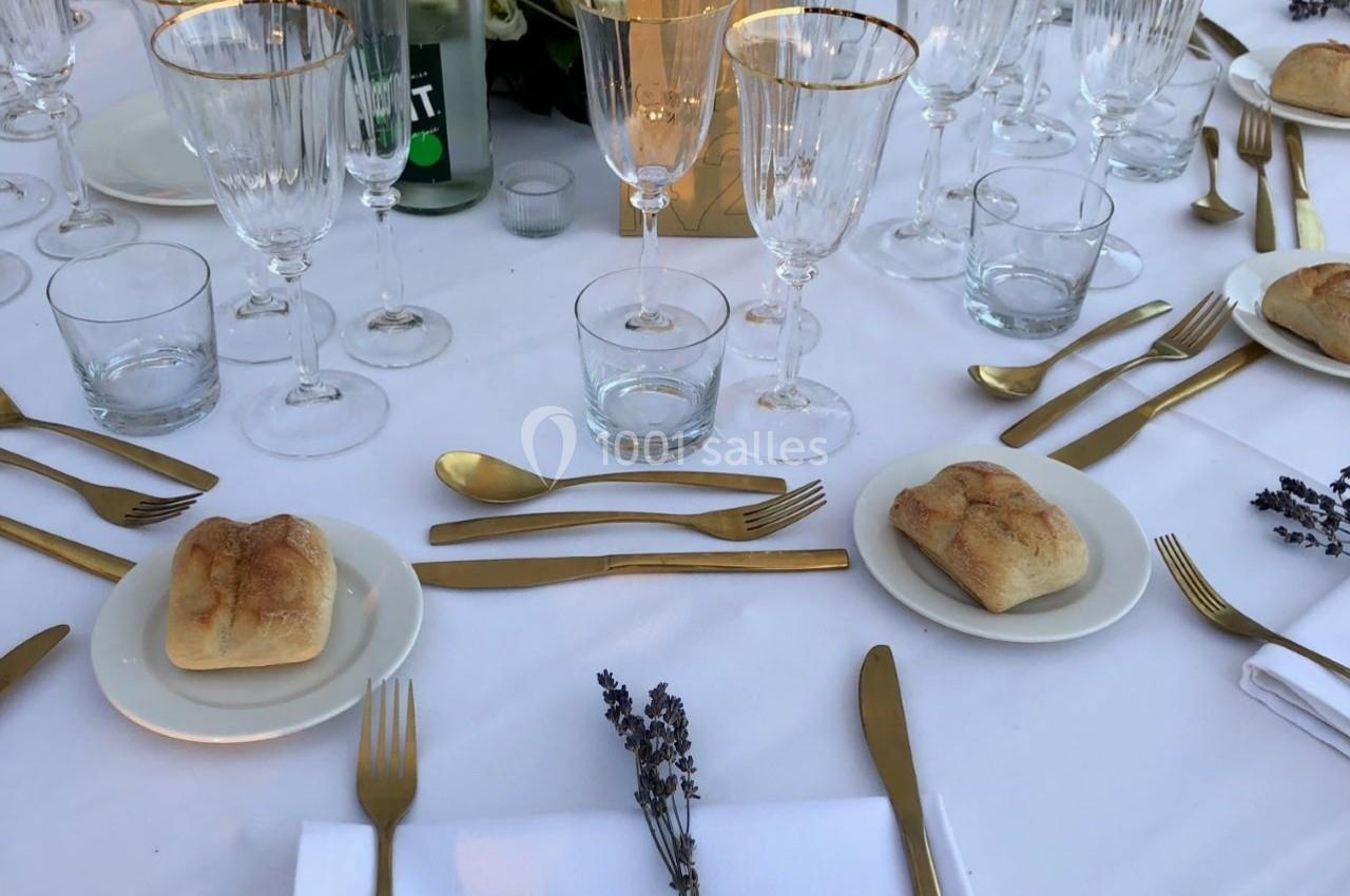 Table dressée avec vaisselle élégante, couverts dorés, verres, pains individuels et décoration de lavande.