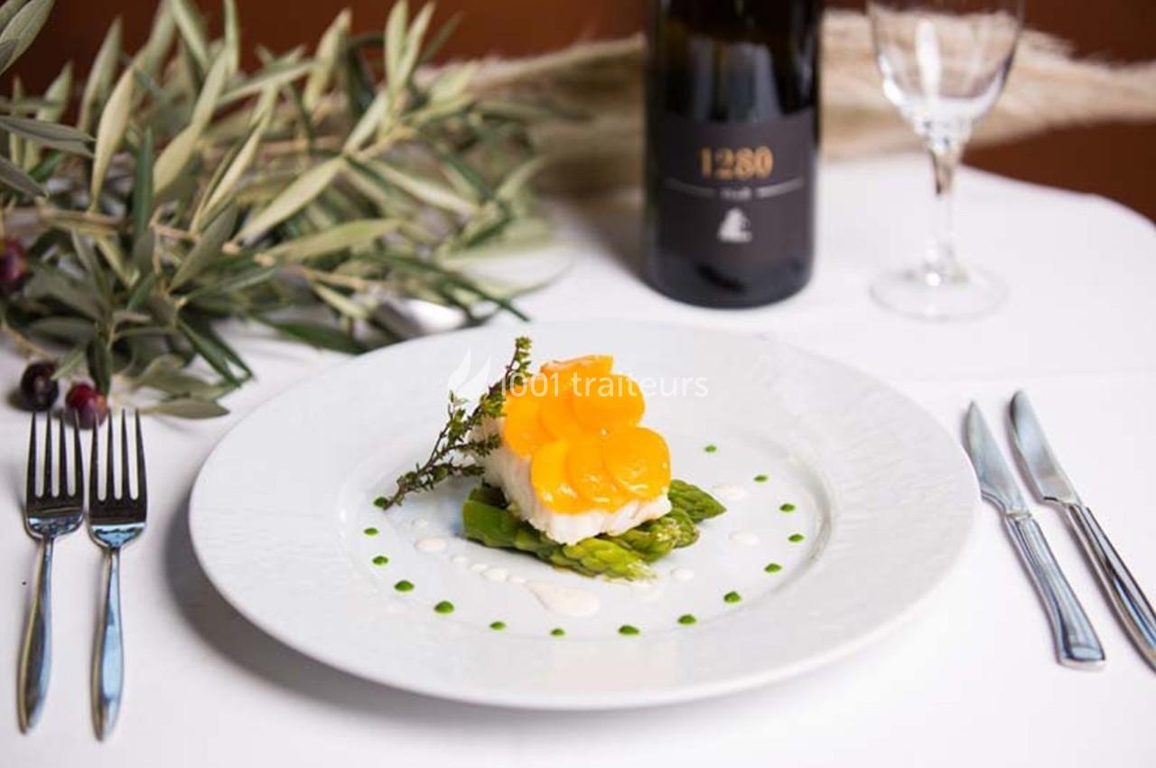 Assiette gastronomique avec asperges, poisson et tranches de légumes jaunes, accompagnée d'une bouteille de vin rouge.