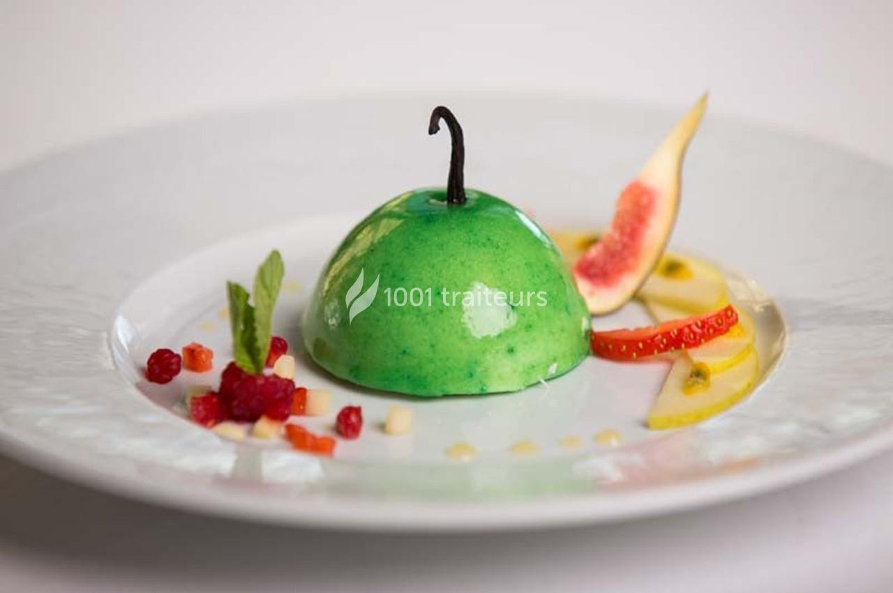 Dessert en forme de pomme verte avec une décoration de fruits frais et une gousse de vanille sur une assiette blanche.