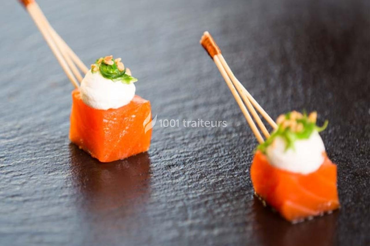 Deux bouchées de saumon cru surmontées de crème et d'herbes, présentées avec des piques en bois sur une ardoise noire.