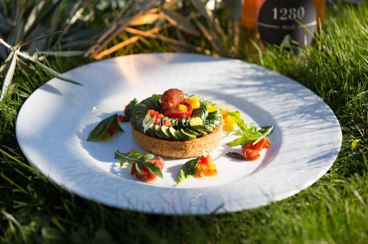 Tartelette garnie de légumes colorés et d'avocat, présentée sur une assiette blanche posée sur de l'herbe.