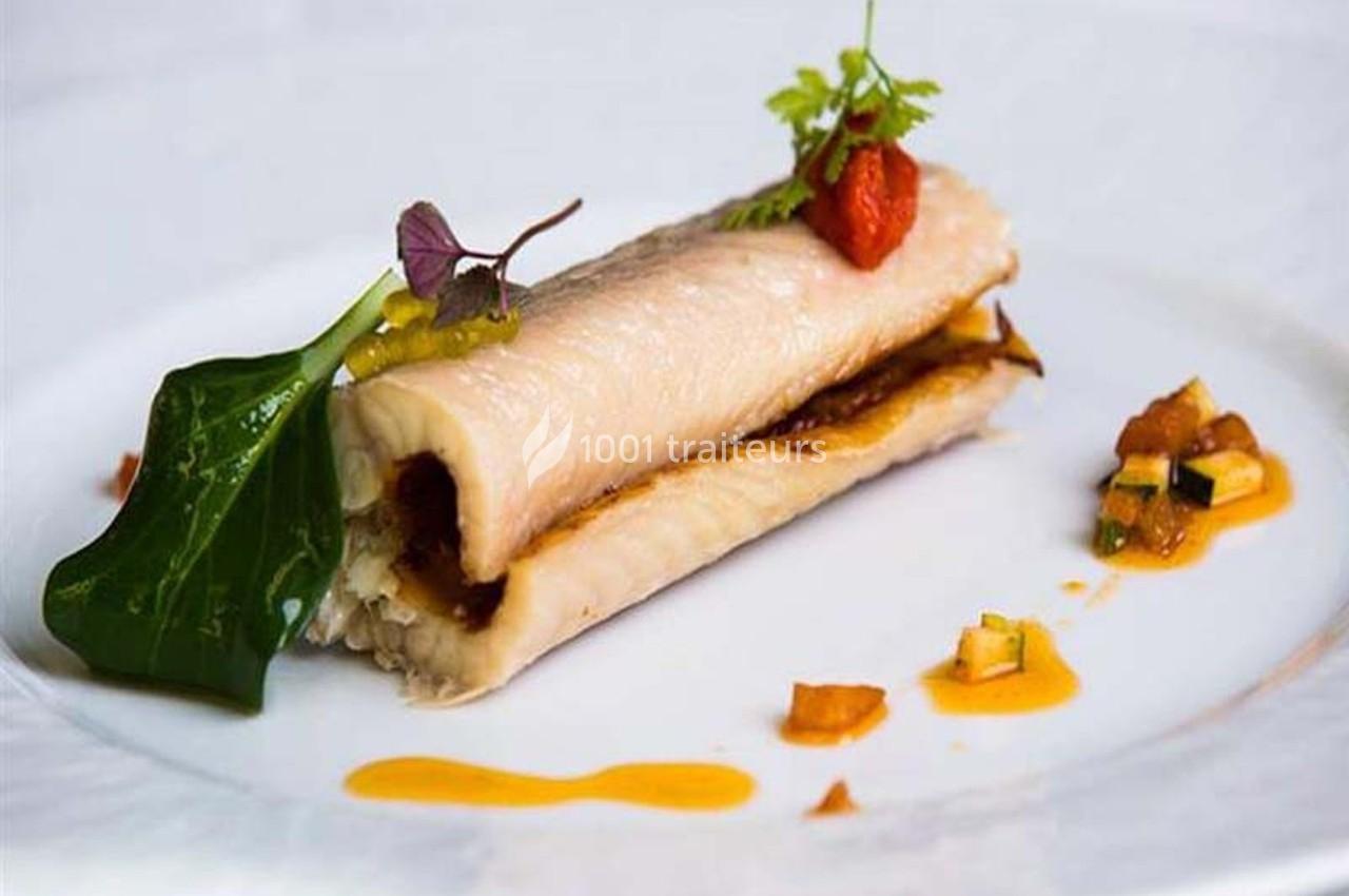 Rouleau de poisson garni de légumes, présenté sur une assiette avec une sauce et des herbes décoratives.