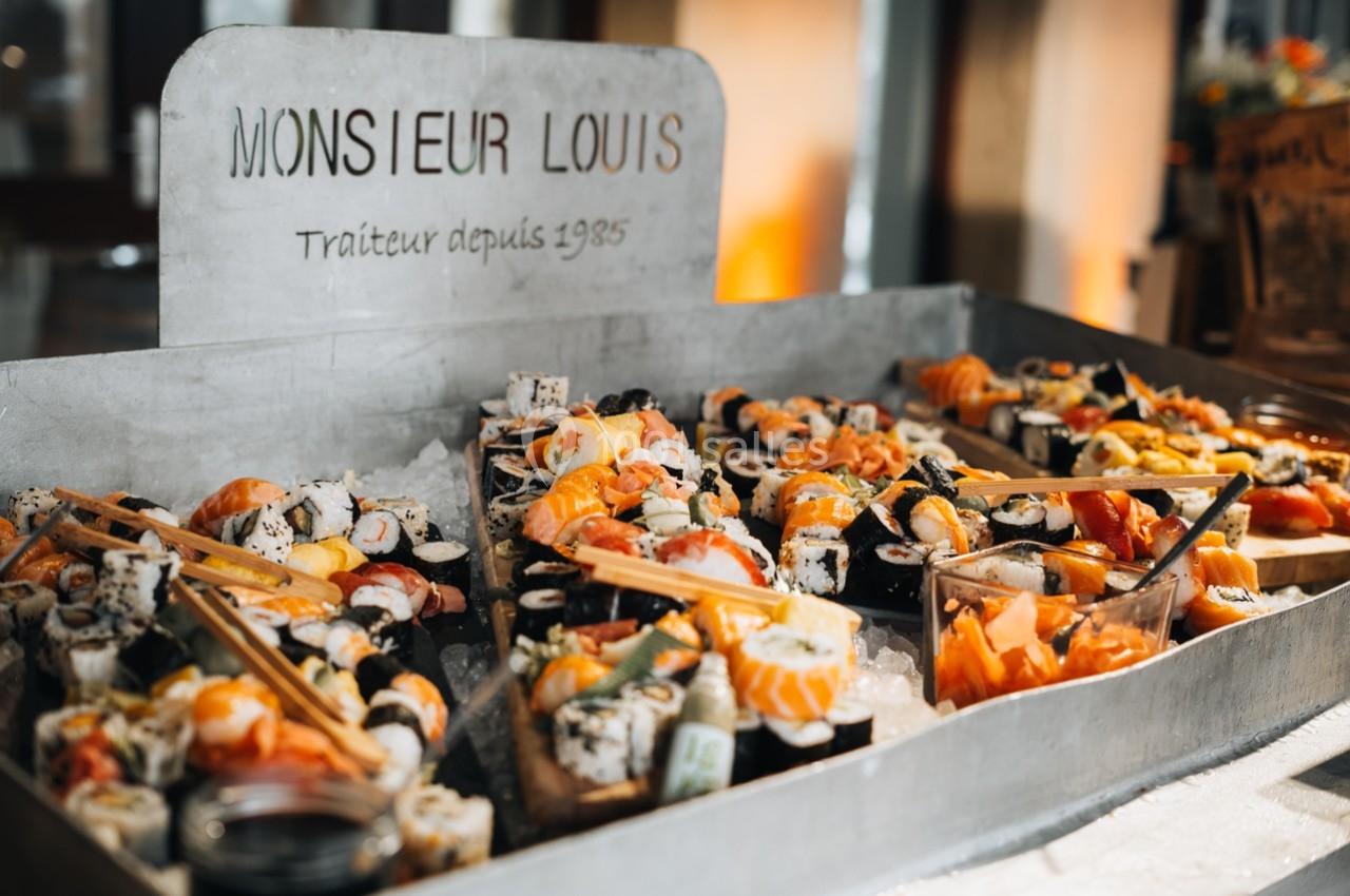 Plateau de sushis variés avec garnitures, présenté sur un comptoir en métal sous une enseigne ’Monsieur Louis’.