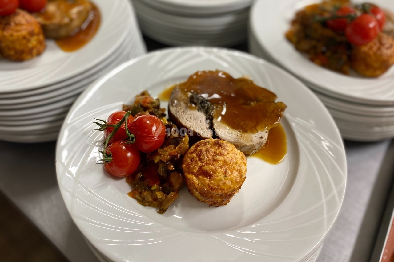 Assiette contenant une tranche de viande en sauce, des tomates cerises rôties, un gratin individuel et des légumes.